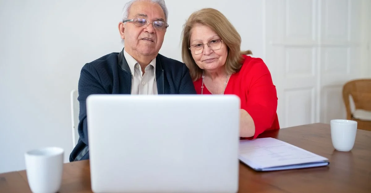 Couple âgé utilisant un ordinateur portable à la maison, partageant un moment chaleureux et intime en ligne.
