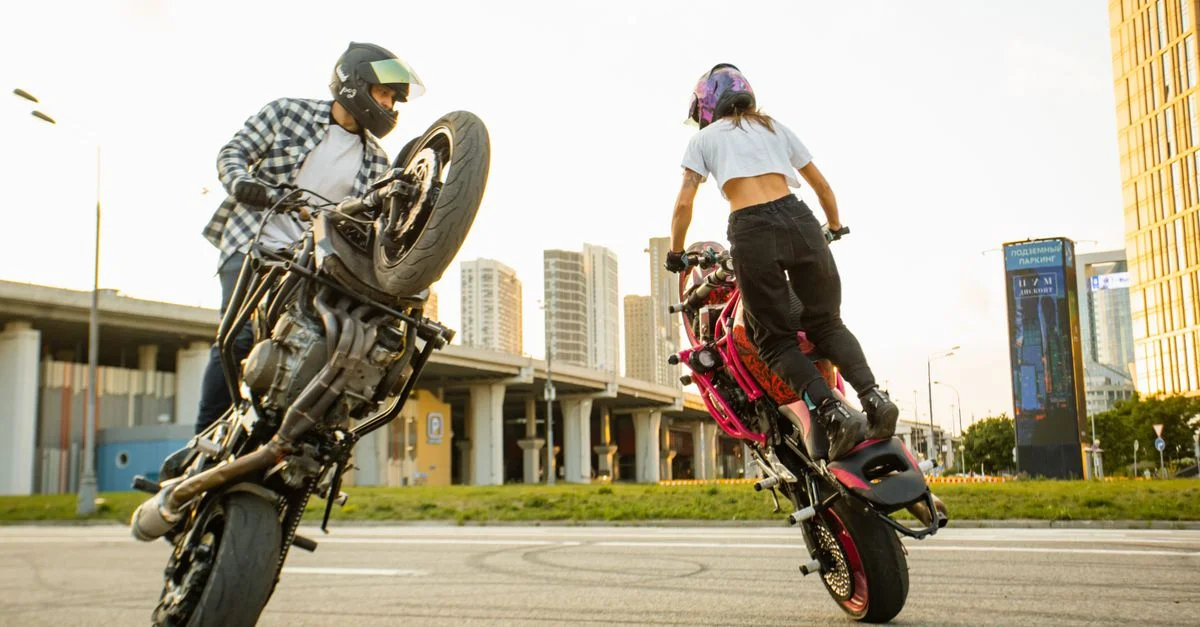 Deux motards effectuant des cascades en moto dans un paysage urbain.