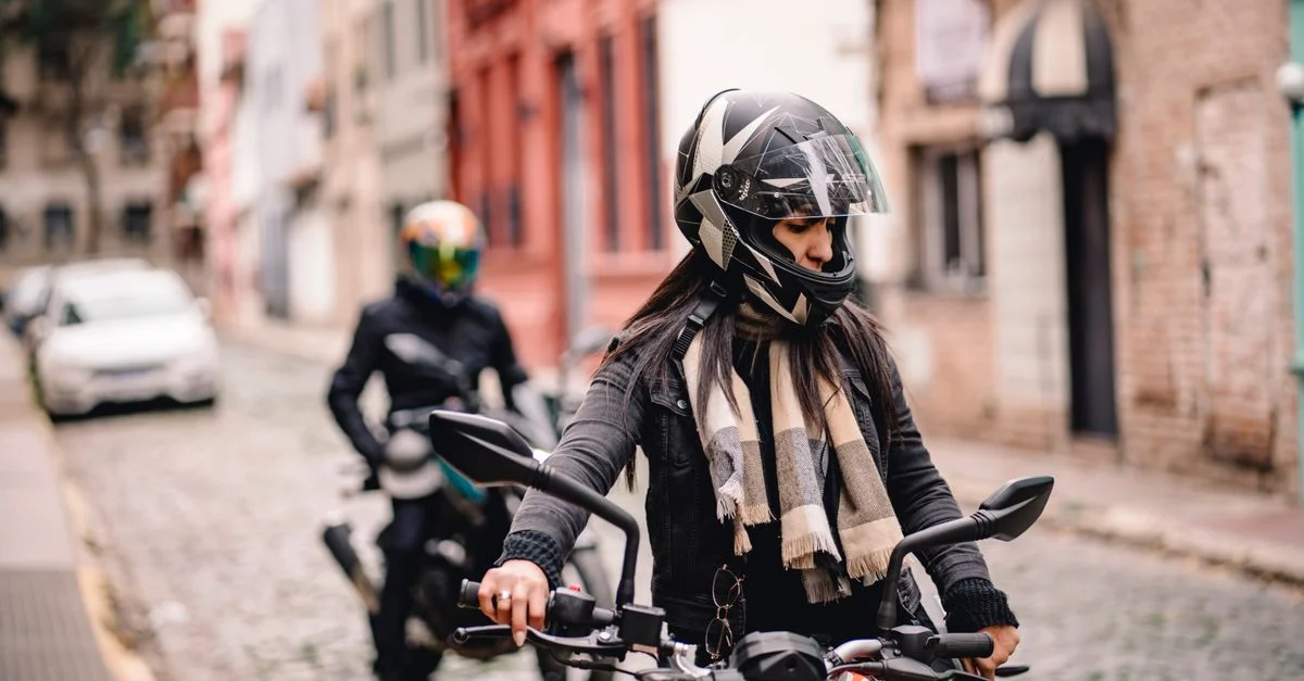 Deux motards en casques naviguent dans une rue pavée de la ville, mettant en avant la mode urbaine de la moto.
