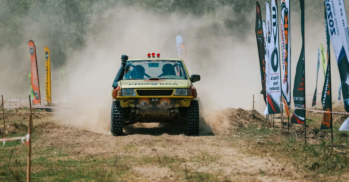 Scène de course tout-terrain dynamique avec un véhicule soulevant la poussière au milieu des drapeaux et des spectateurs.