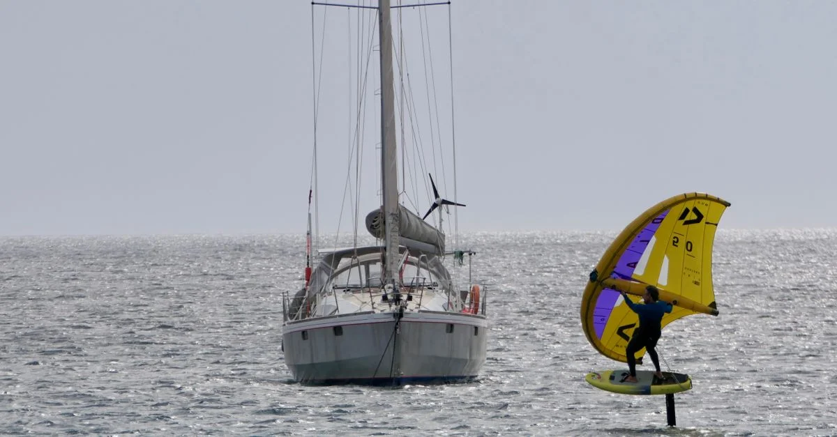 Une scène palpitante d'un homme pratiquant le wingfoil près d'un voilier en mer ouverte.