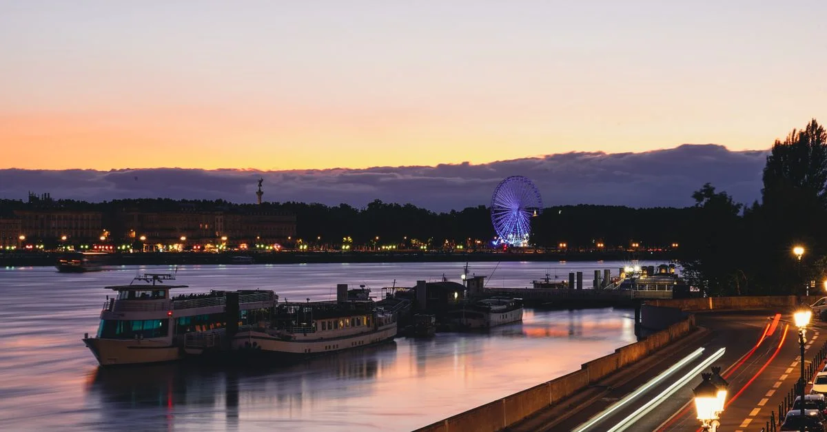 Magnifique panorama du soir de la Garonne à Bordeaux avec grande roue illuminée et navires à quai.