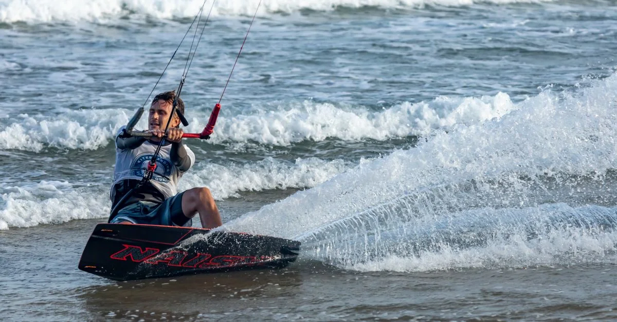 Homme faisant du kitesurf avec enthousiasme sur l'océan avec des vagues éclaboussant autour de lui.
