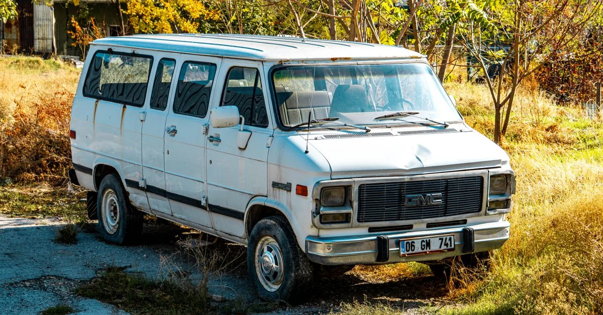 Une vieille camionnette blanche garée dans un terrain envahi par la végétation avec un feuillage d'automne.