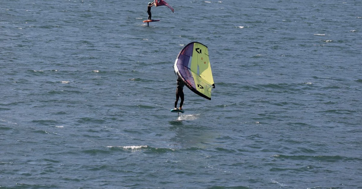 Deux personnes pratiquent le wingfoil sur le lac de Garde, en Italie, une destination prisée pour les sports nautiques.