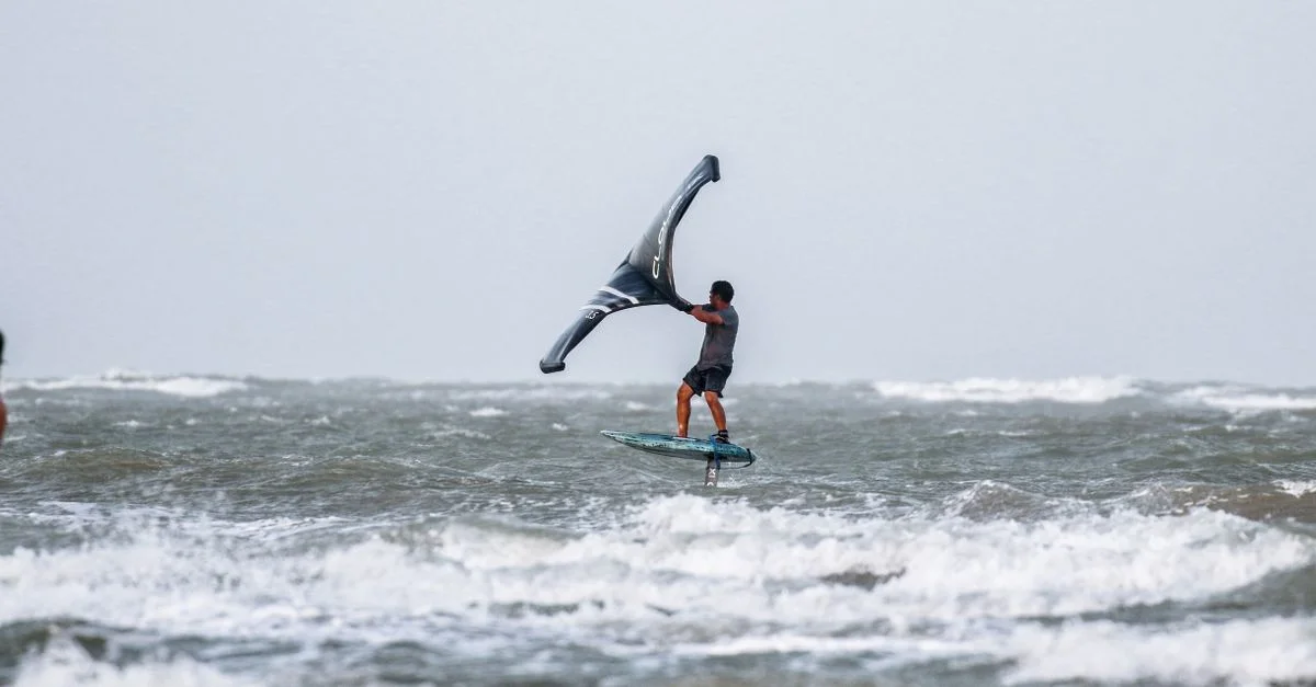 Une prise de vue captivante d'un homme faisant du wing foil sur les vagues de l'océan, mettant en avant aventure et compétence.